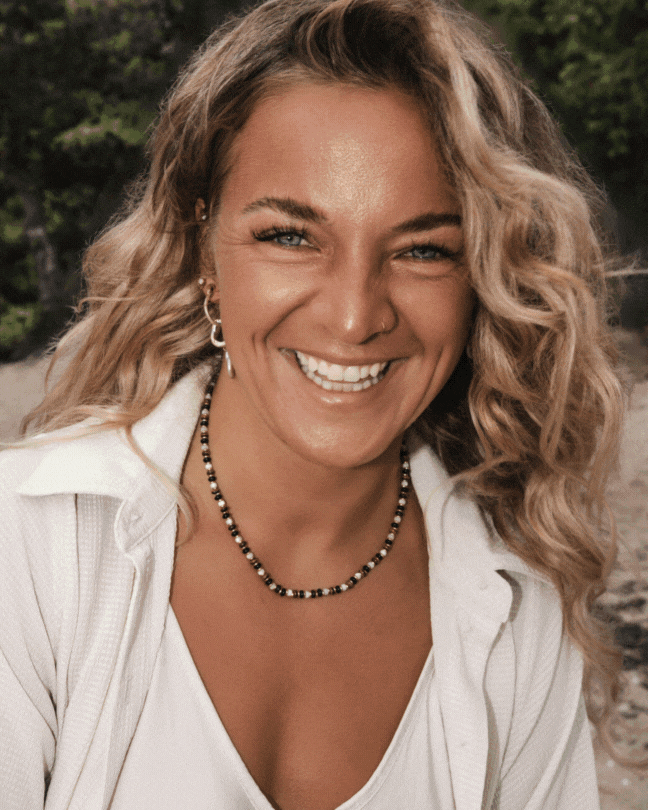 Thekla Matei smiling in the camera with white clothing and beautiful jewelry with ocean mood and the Triada Designs Logo