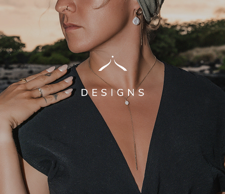 Thekla Matei with a black shirt and a beautiful long necklace, earrings and rings on the shore. The Triada Designs Logo Is infront